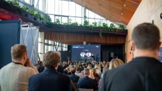 Audience seated in a modern atrium-style conference hall watching a stage presentation with a large screen that reads FutureLAW '26 and hosts on stage.