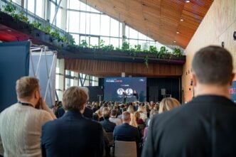 Audience seated in a modern atrium-style conference hall watching a stage presentation with a large screen that reads FutureLAW '26 and hosts on stage.