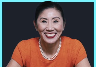 Smiling woman in an orange top with a pearl necklace, against a dark backdrop and bright turquoise border.