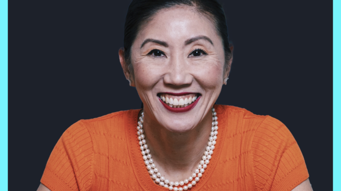 Smiling woman in an orange top with a pearl necklace, against a dark backdrop and bright turquoise border.